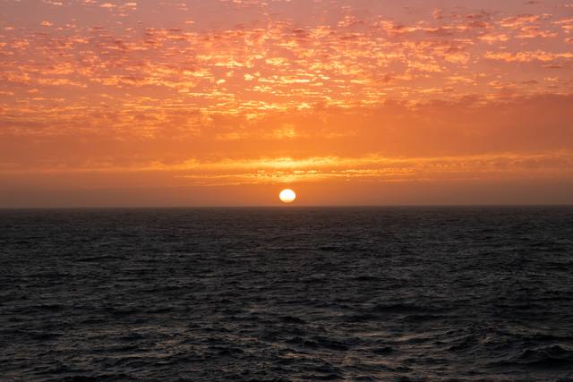 The sun sets under orange clouds above a calm sea.