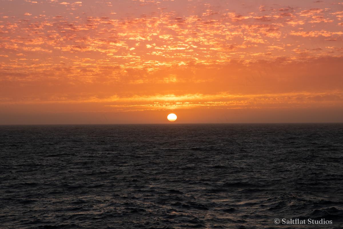 The sun sets under orange clouds above a calm sea.